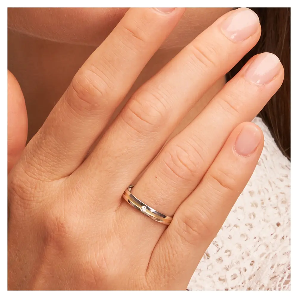 Gelbgold und Weissgold Ehering mit Diamanten und sandmattem streifen auf Hand am Gesicht im Zoom