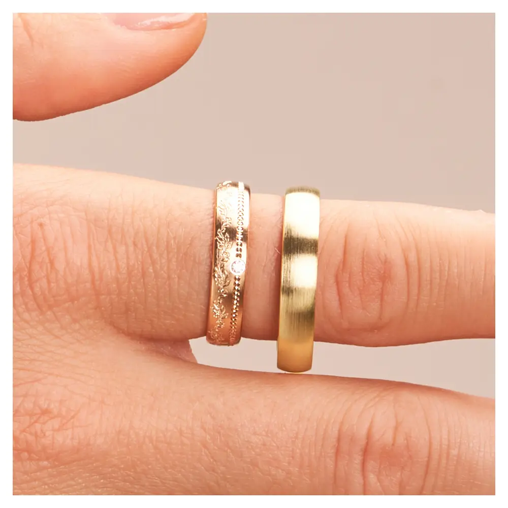 Mattierte Eheringe aus Gelbgold mit Diamanten und Blumenmuster im Damenring auf Finger