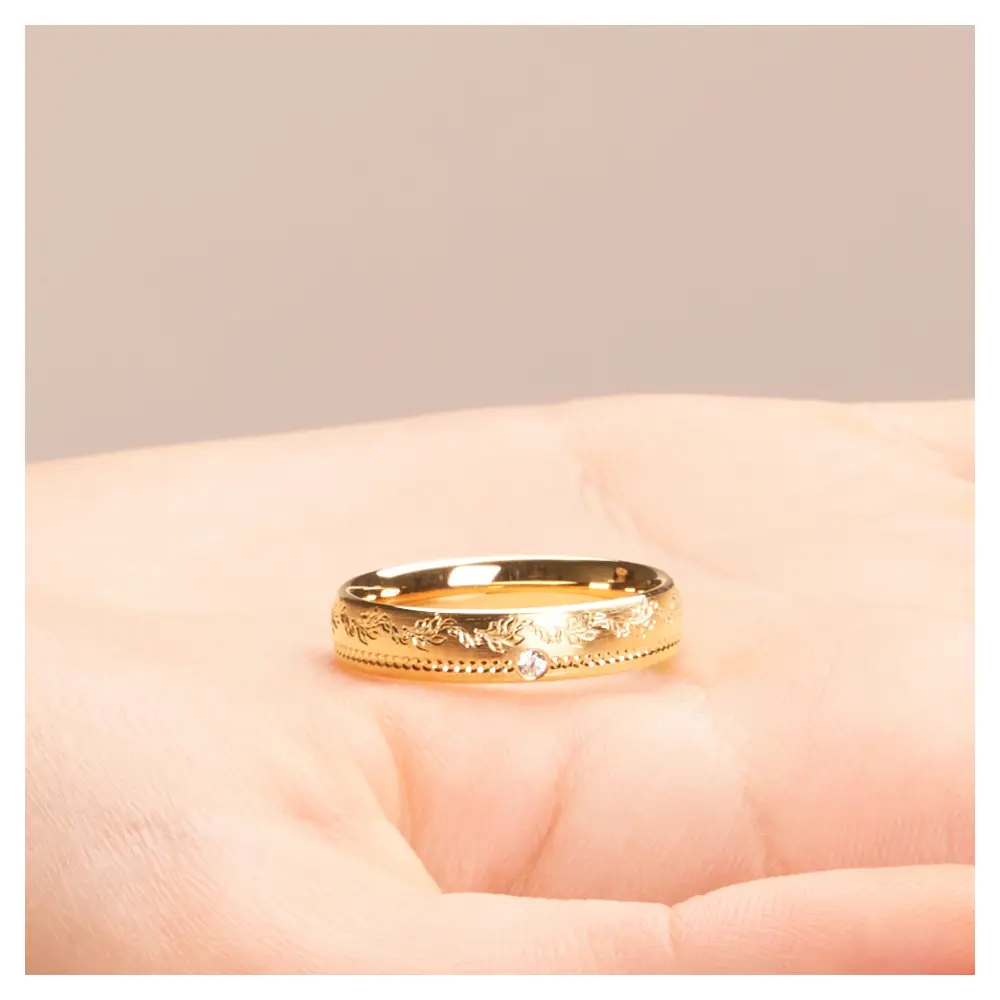 Mattierter Ehering aus Gelbgold mit Diamanten und Blumenmuster auf Hand liegend