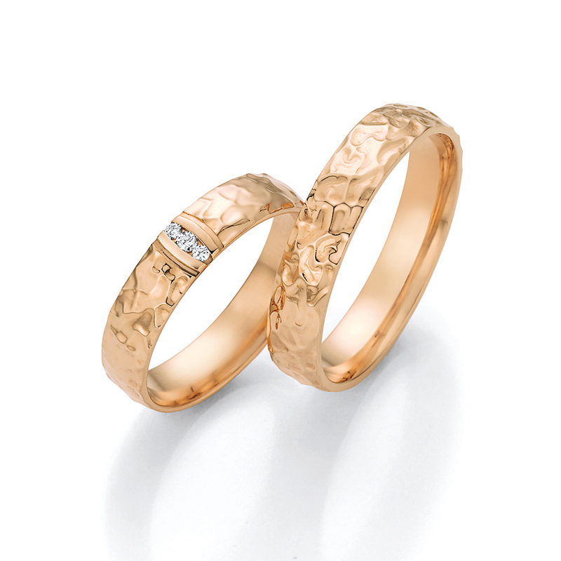 Aufnahme von Trauringen aus Roségold in zerknitterter Optik mit drei Diamanten