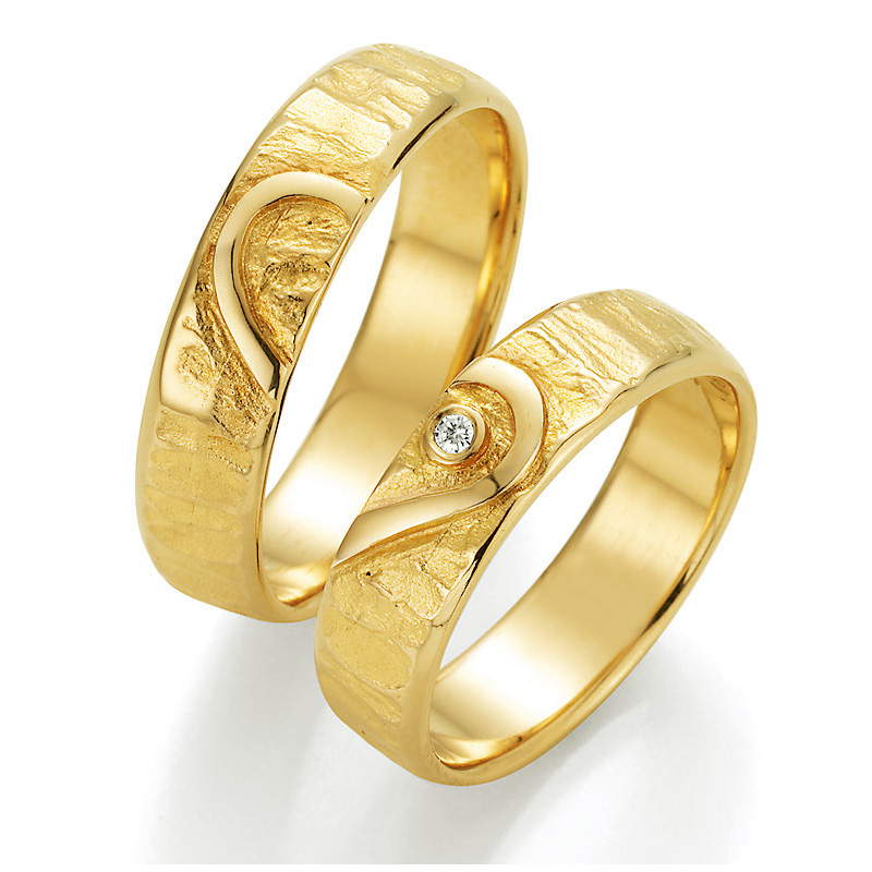 Seitliche Aufnahme von strukturierten Trauringen aus Gelbgold mit Herzmuster und Diamant im Herz