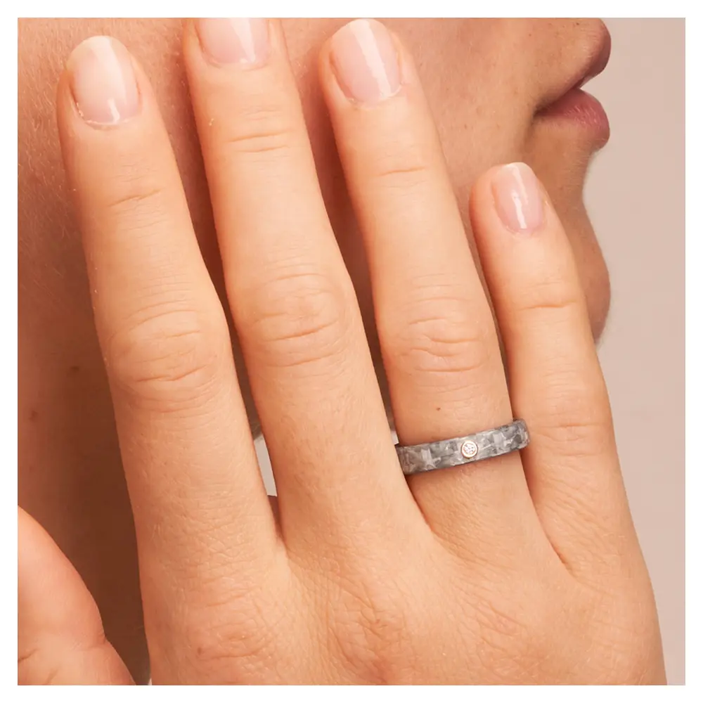 Eheringe aus grauem Carbon mit Diamanten in Rotgoldfassung auf Hand am Gesicht im Zoom