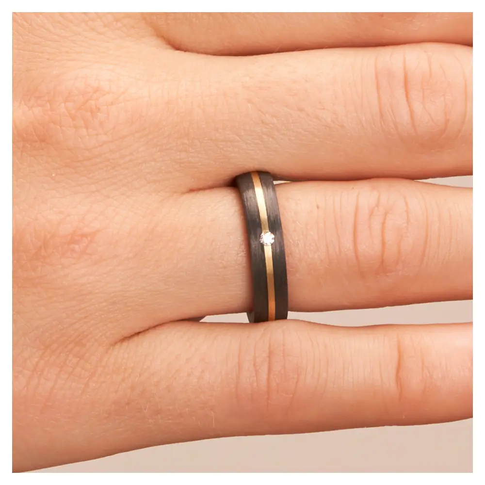 Eheringe aus Carbon mit Diamanten und Gelbgoldstreifen auf Hand im Zoom