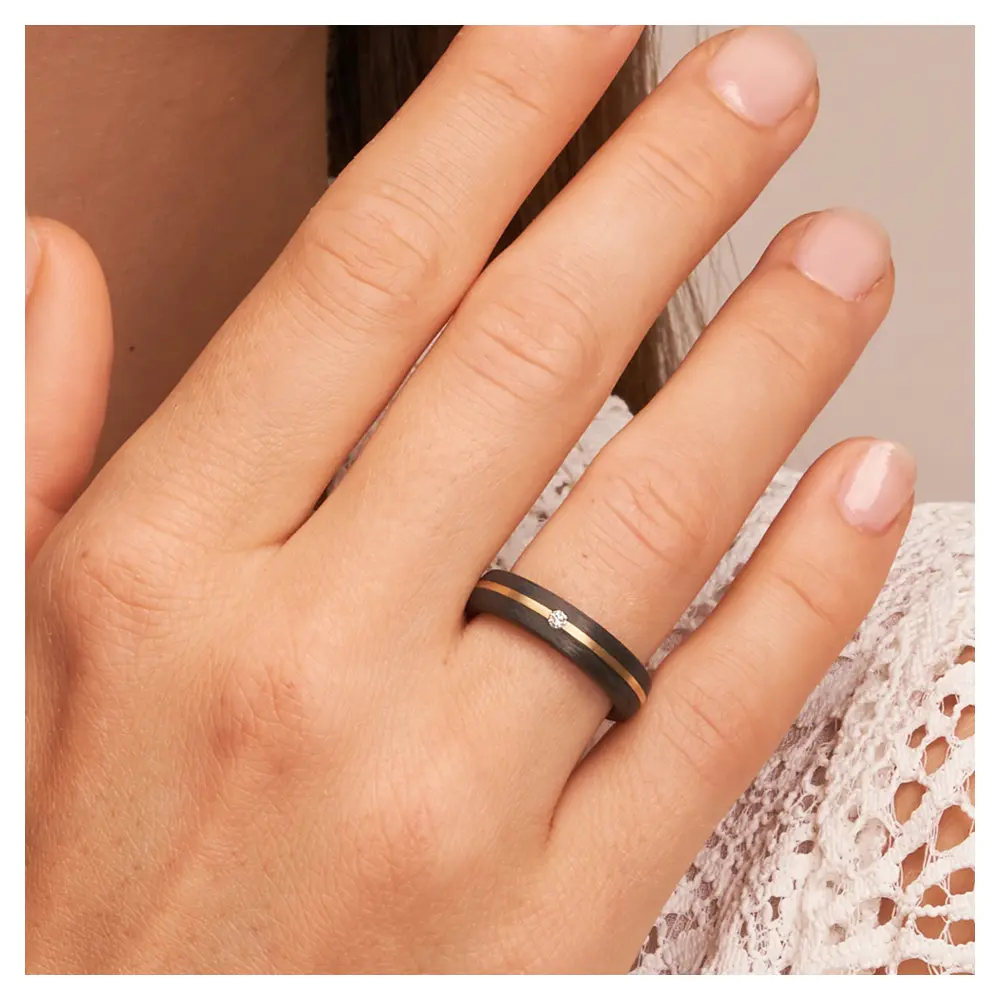 Eheringe aus Carbon mit Diamanten und Gelbgoldstreifen auf Hand im Gesicht im Zoom