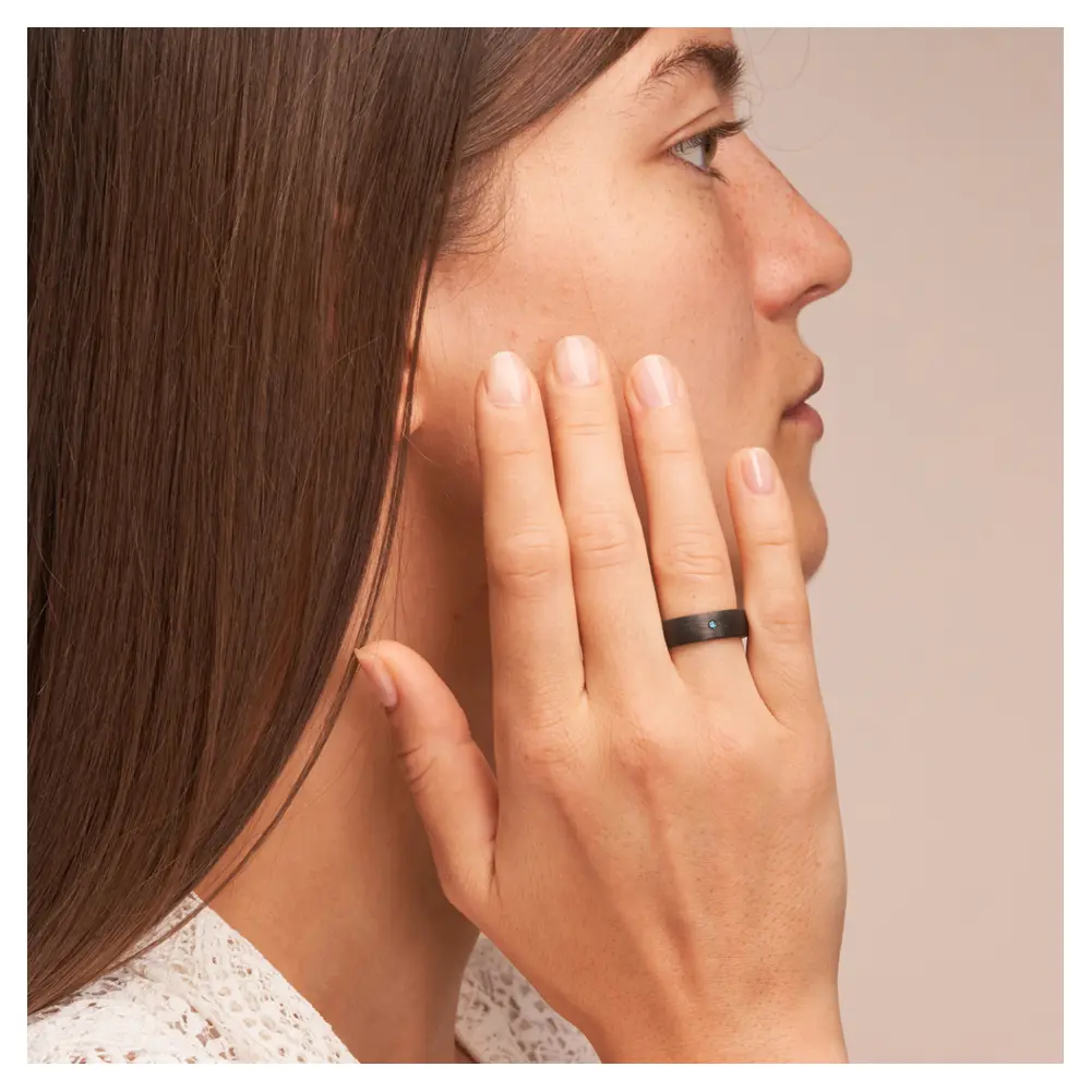 Ehering aus Carbon mit blauem Diamanten auf Hand
