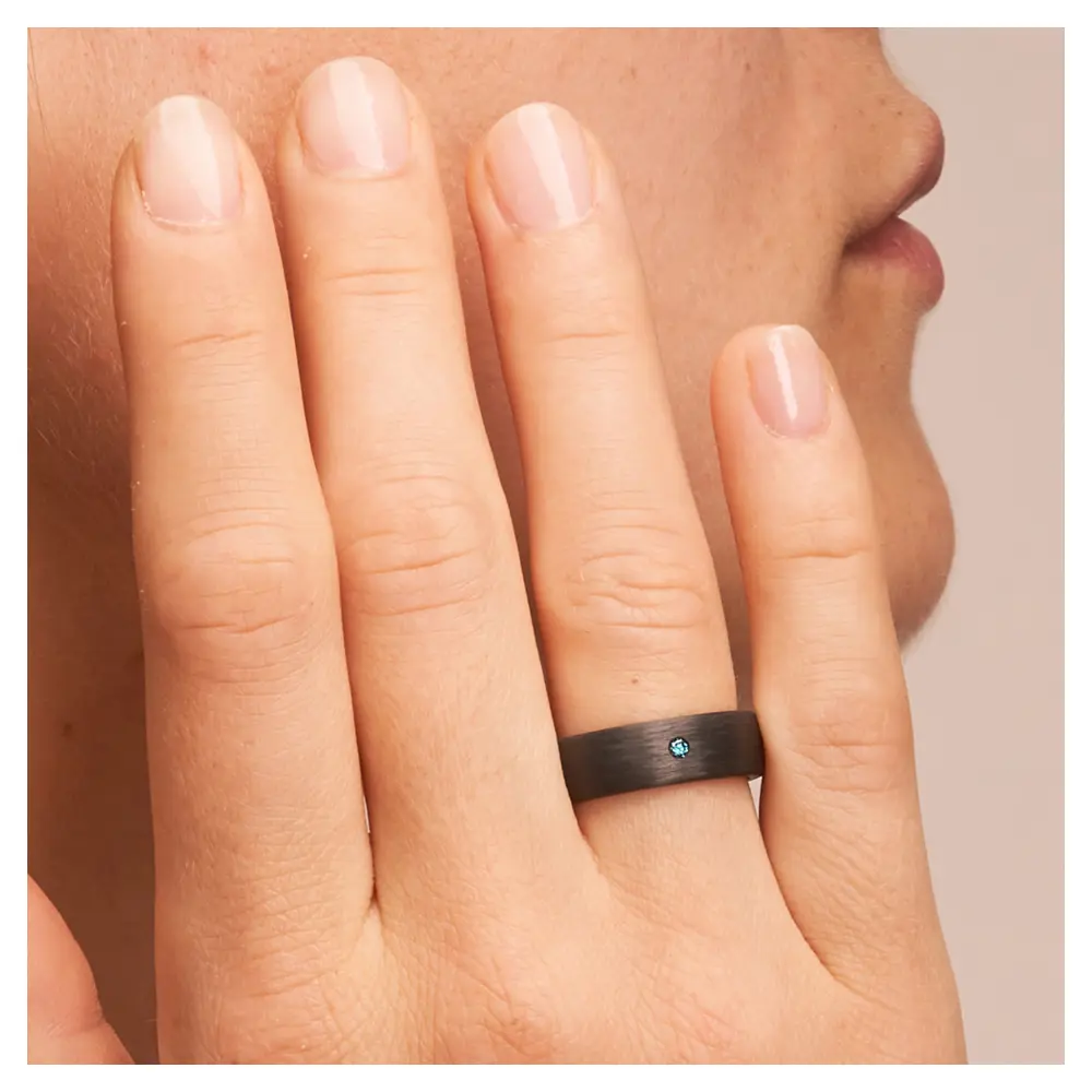 Ehering aus Carbon mit blauem Diamanten auf Hand im Zoom