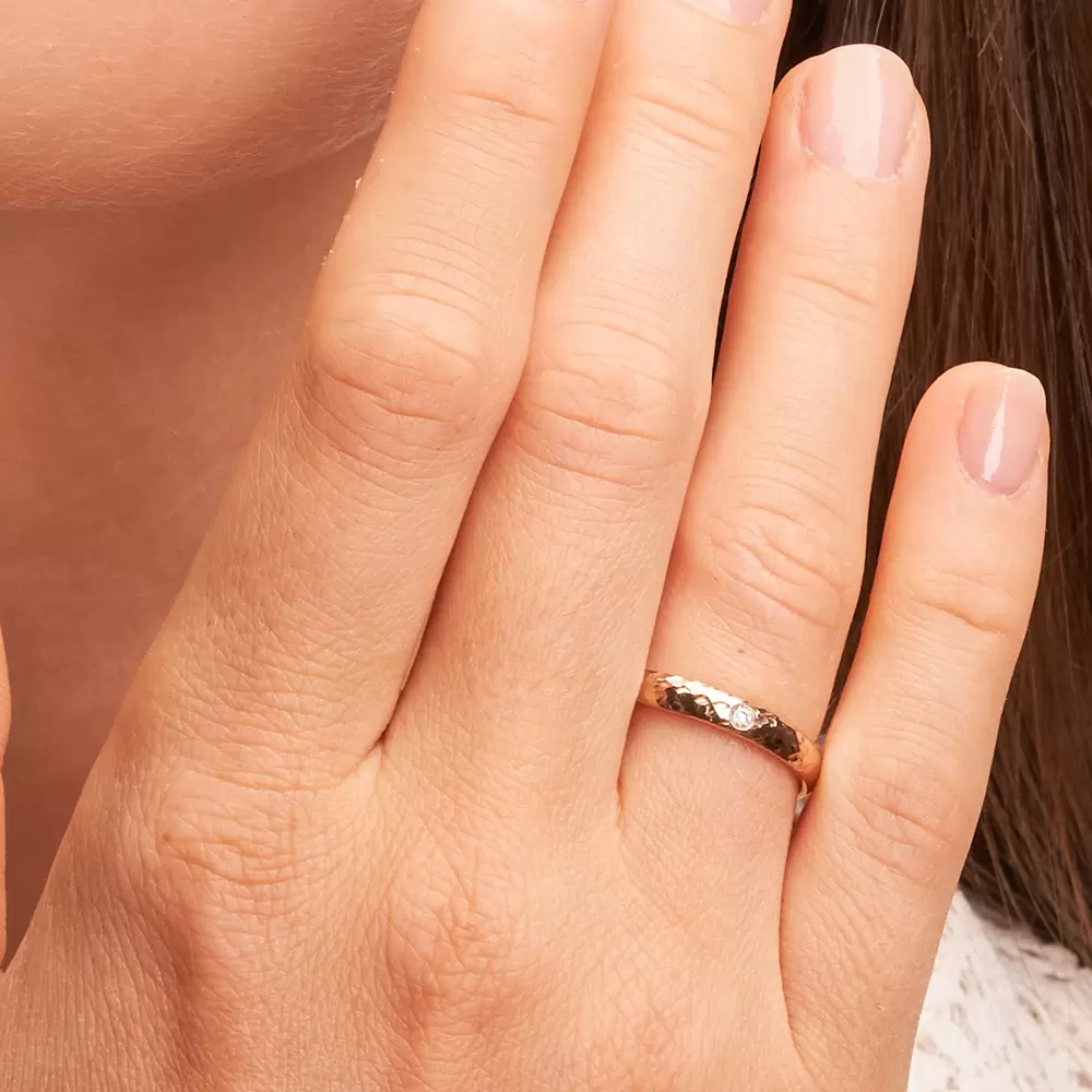 Ehering aus Herbstgold mit 0,03 Karat Diamanten und Hammerschlag auf Hand im Zoom