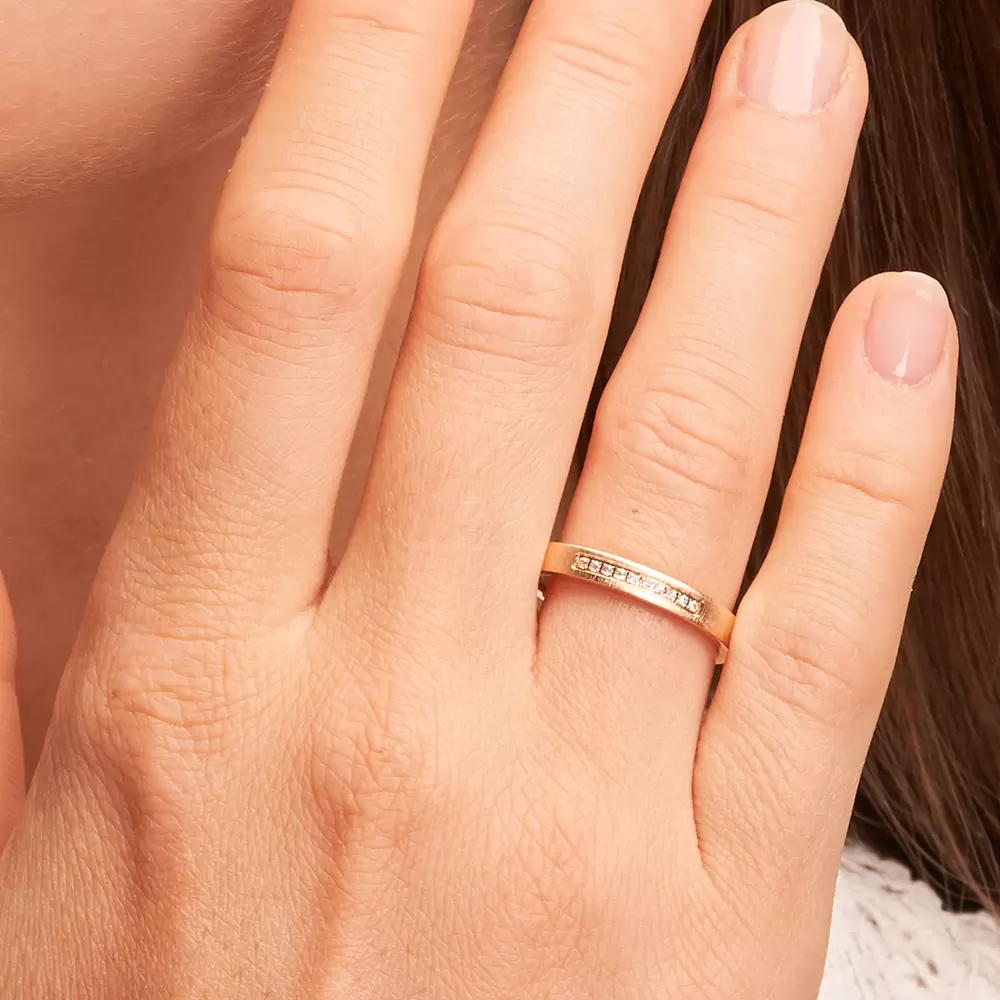 Außen flache Eheringe aus quermattem Sommergold mit Diamantenreihe auf Hand im Zoom
