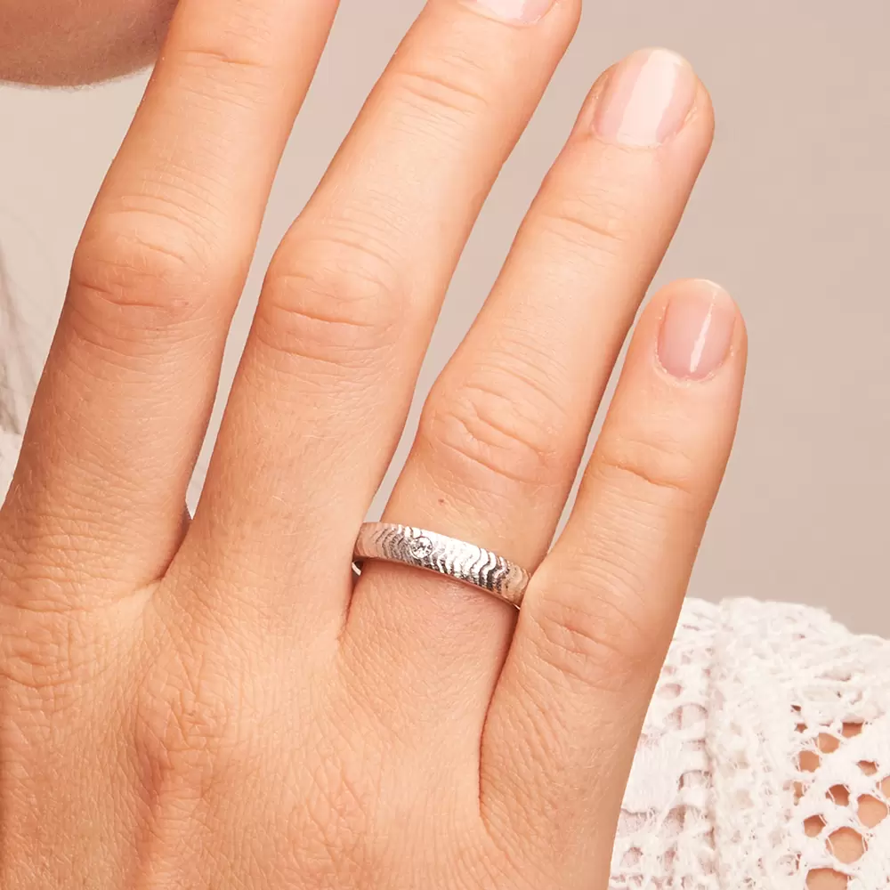 Eheringe aus strukturiertem Weißgold mit 0,04 Karat Diamanten auf Hand im Zoom