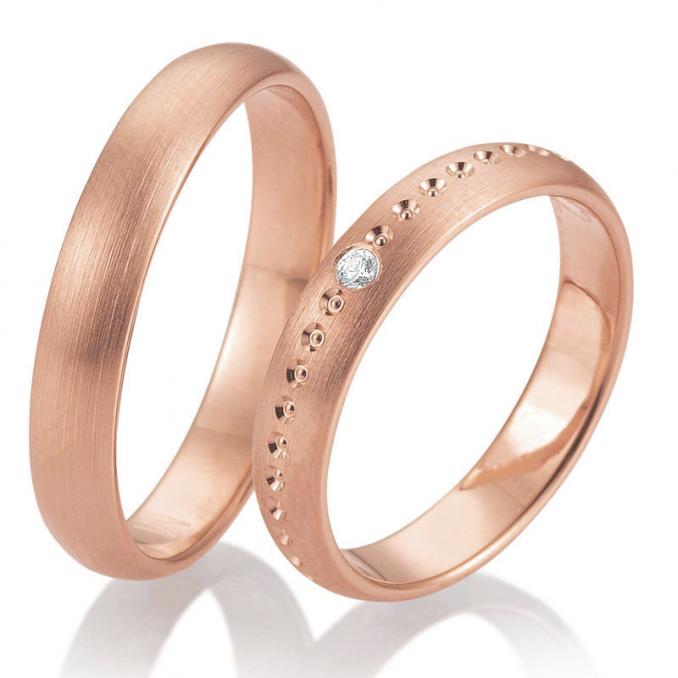 Seitliche Aufnahme von gerundeten Trauringen aus Roségold mit einem Diamanten und Kreismuster 