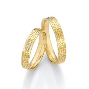 Aufnahme von Trauringen aus Gelbgold mit Puzzlemuster und drei weißen Diamanten