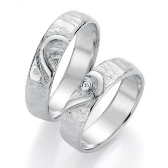 Seitliche Aufnahme von strukturierten Trauringen aus Weissgold mit Herzmuster und Diamant im Herz